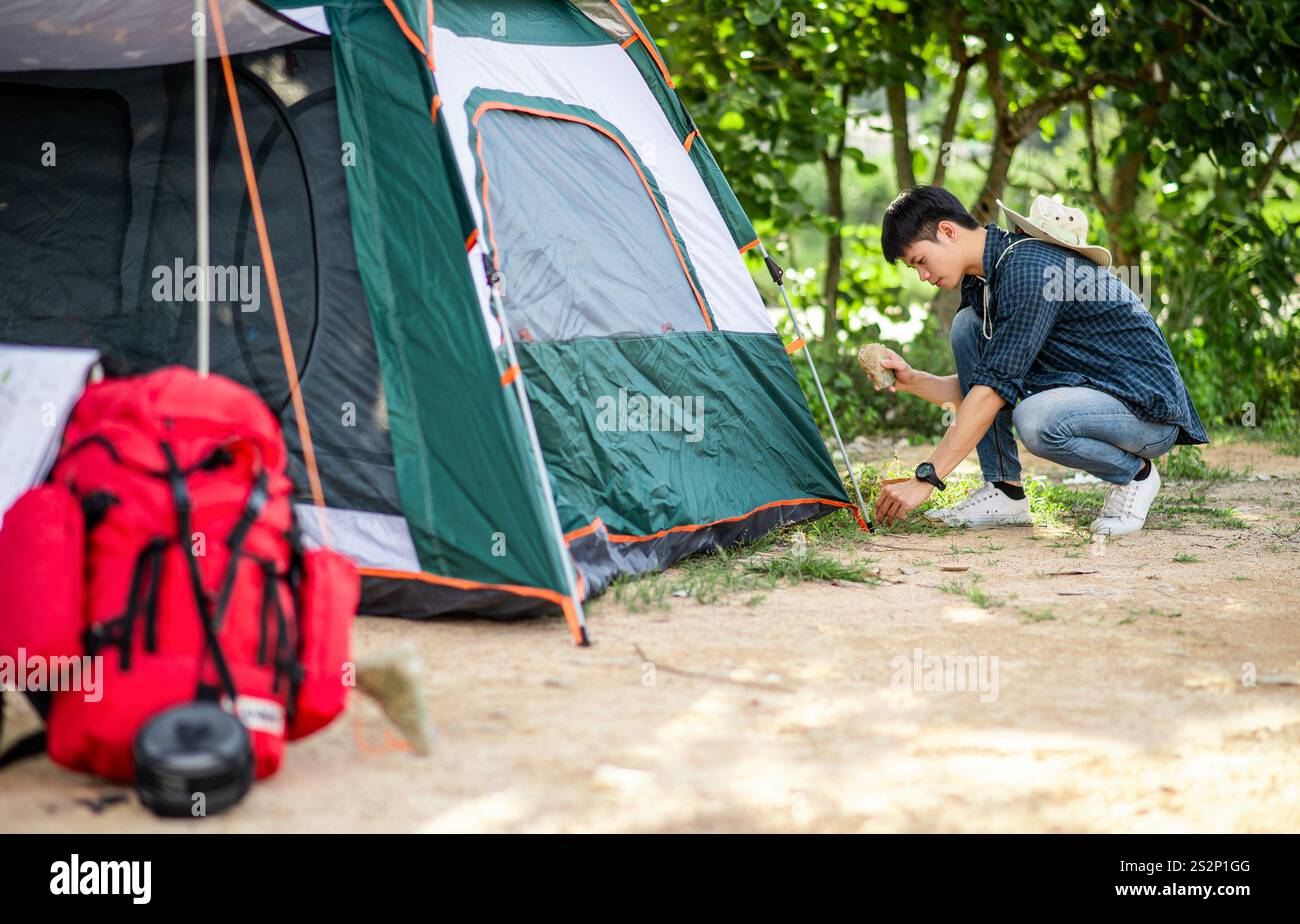 Il giovane viaggiatore usa uno stoneto sulle tenda nella foresta mentre campeggia in vacanza estiva Foto Stock