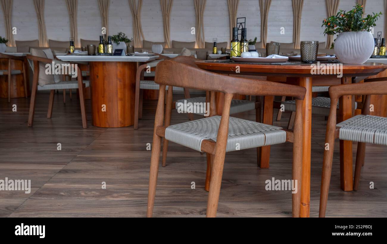 Un elegante ristorante interno allestito con sedie in legno e tavoli rotondi, caratterizzato da decor moderno, illuminazione soffusa e un'atmosfera intima. Foto Stock