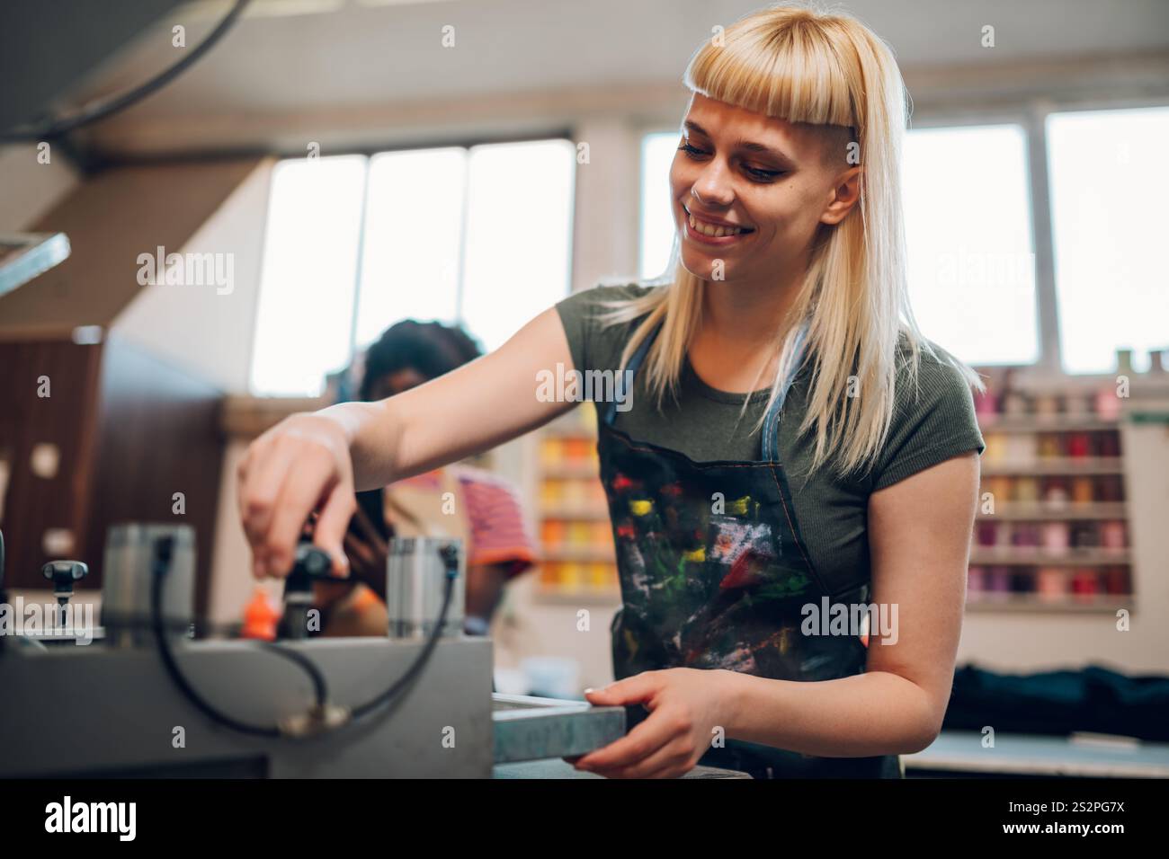 Ritratto di un tecnico grafico sorridente in piedi presso l'officina di stampa e che manipola la macchina per la stampa serigrafica. Tipografia lavoratrice addetta Foto Stock