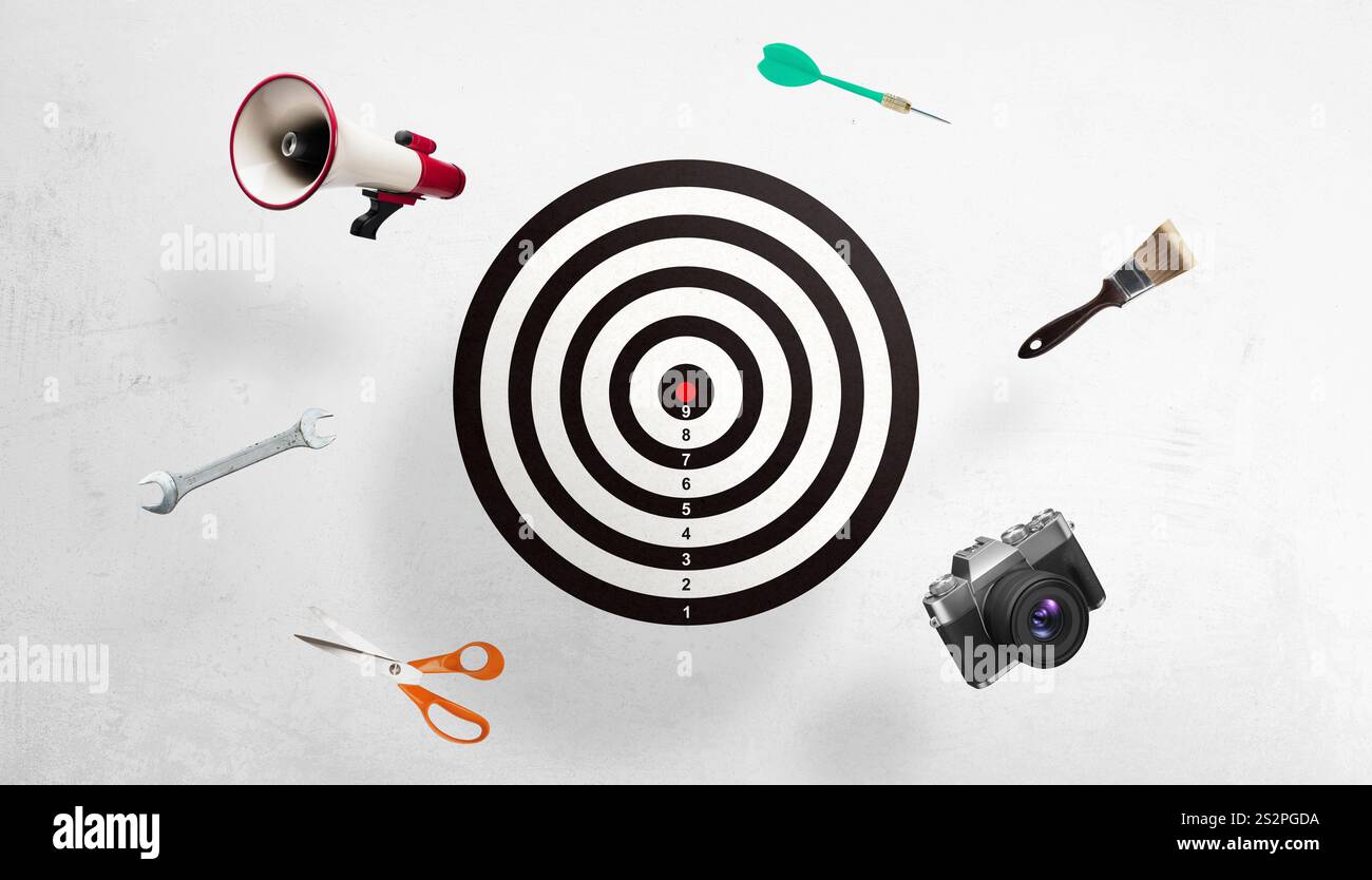 Target in bianco e nero circondato da megafono, freccette, pennello, fotocamera, forbici, e chiavi in mano, simboleggiano una campagna di marketing e un obiettivo creativo Foto Stock