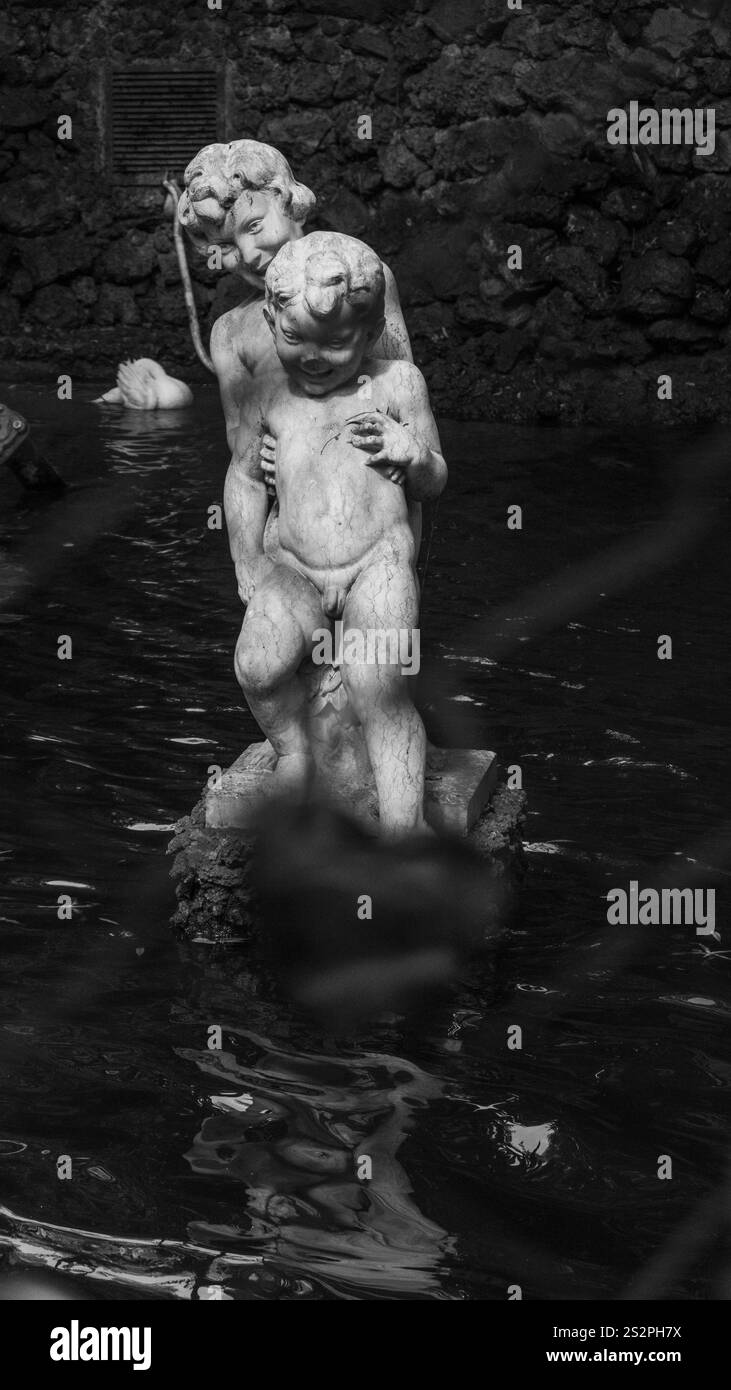 Un'immagine in bianco e nero di una classica statua in marmo raffigurante due figure in piedi in uno stagno, circondato da acqua riflettente e un bac in pietra testurizzata Foto Stock
