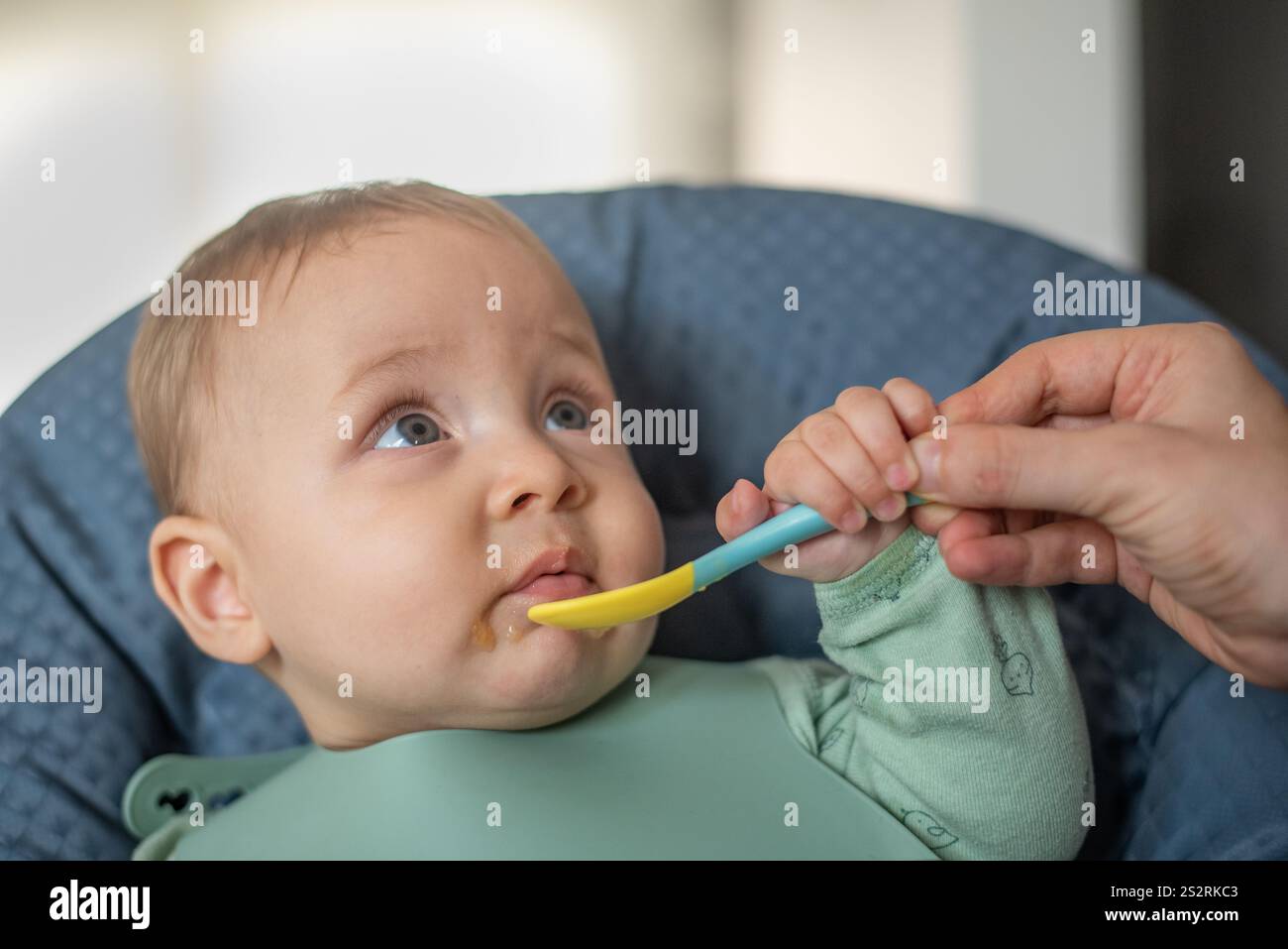 bambino di 6 mesi che inizia a nutrire cibi solidi guardando sua madre che lo sta aiutando Foto Stock