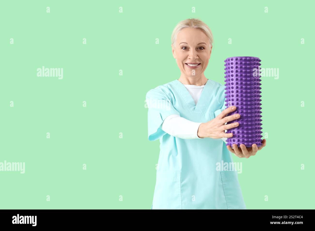 Fisioterapista femminile con rullo in schiuma su sfondo verde Foto Stock