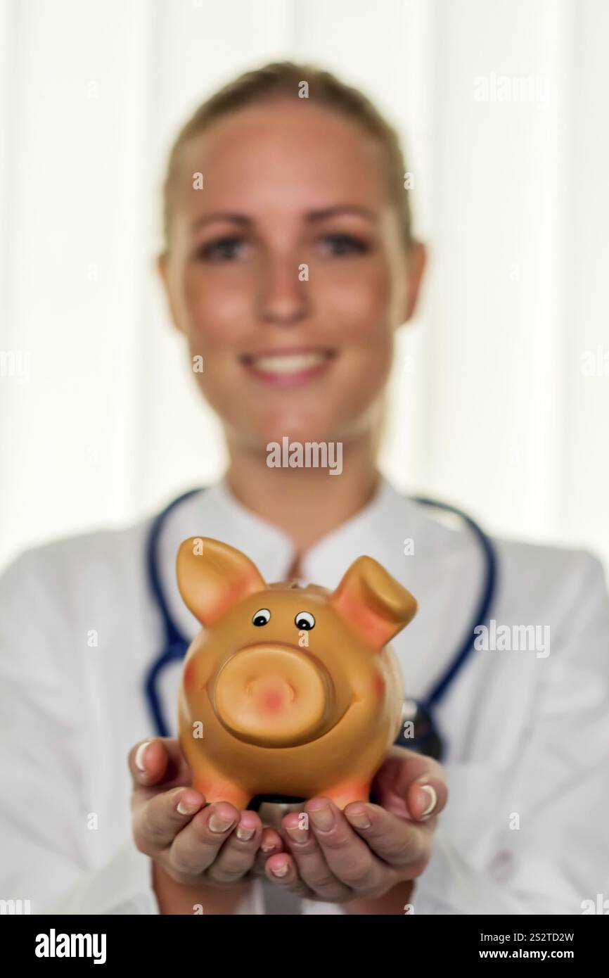 Un giovane medico ha in mano un salvadanaio. Foto simbolica per le tasse del medico, apertura di uno studio e assicurazione pensionistica. Austria Foto Stock