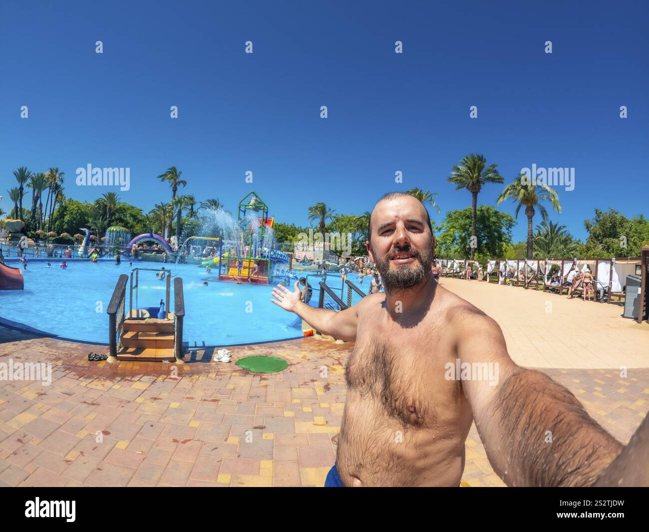 Turista che si gode una vacanza estiva, facendo un allegro selfie in piscina in un vivace parco acquatico sotto il cielo azzurro Foto Stock