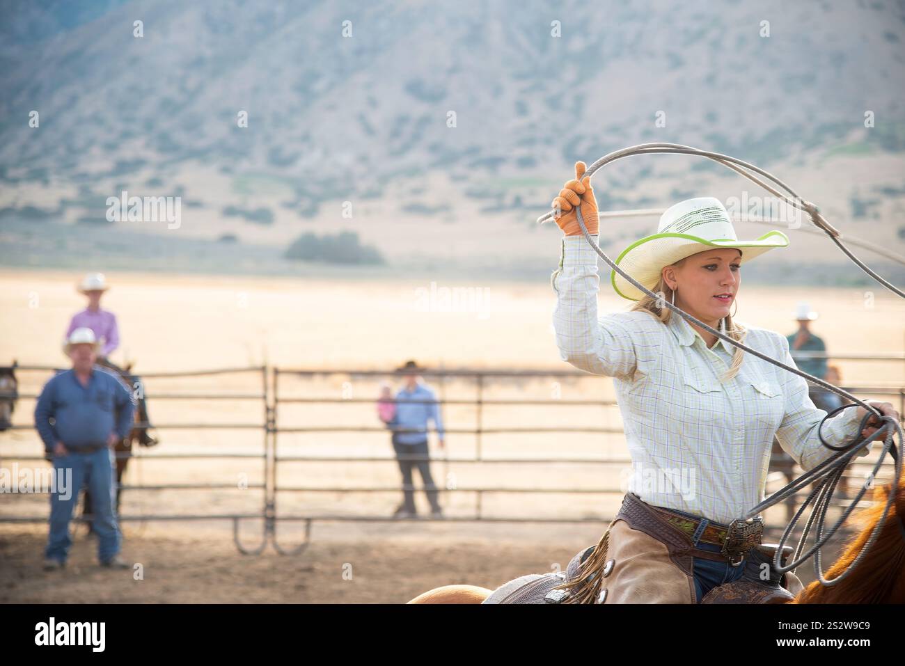 Un'abile cowgirl comanda l'arena, lazo in mano, mentre una folla impaziente guarda sullo sfondo di maestose montagne e ampie pianure aperte Foto Stock Un'abile cowgirl comanda l'arena, lazo in mano, mentre una folla impaziente guarda sullo sfondo di maestose montagne e ampie pianure aperte Foto Stock