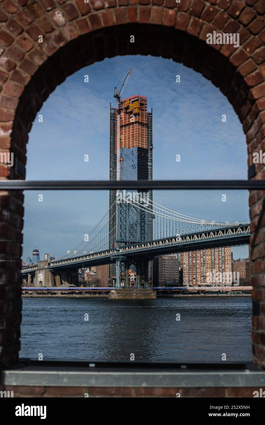 Skyline di Manhattan, tra cui il ponte di Manhattan, l'East River e la costruzione di grattacieli, come si vede dall'arco in mattoni sul lungomare di Brooklyn. Foto Stock