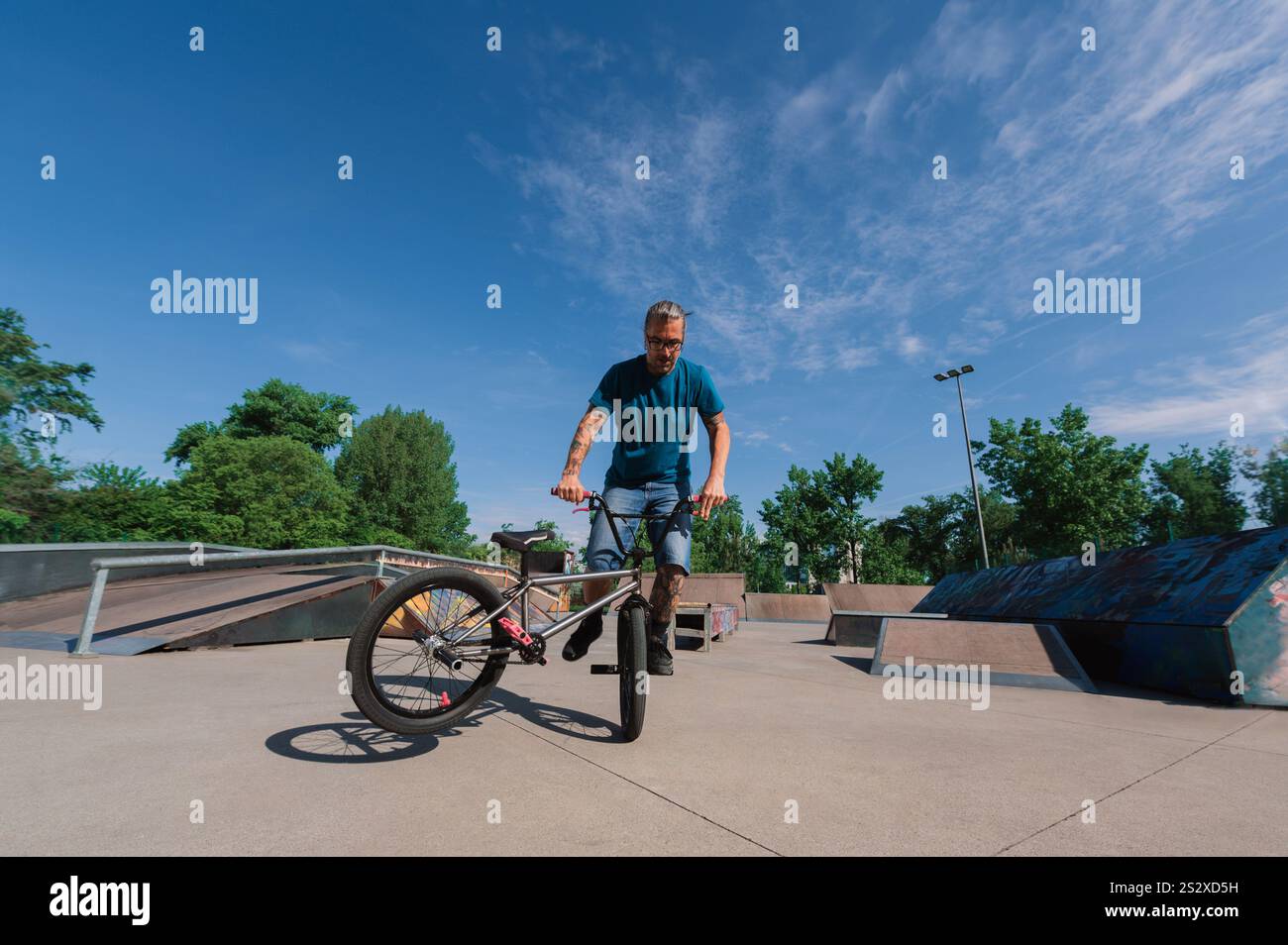 Uno sportivo estremo del Medioevo sta praticando un trick a rotazione 360 sulla sua bmx in uno skate Park. Un ragazzo urbano maturo tatuato sta facendo trucchi freestyle o Foto Stock