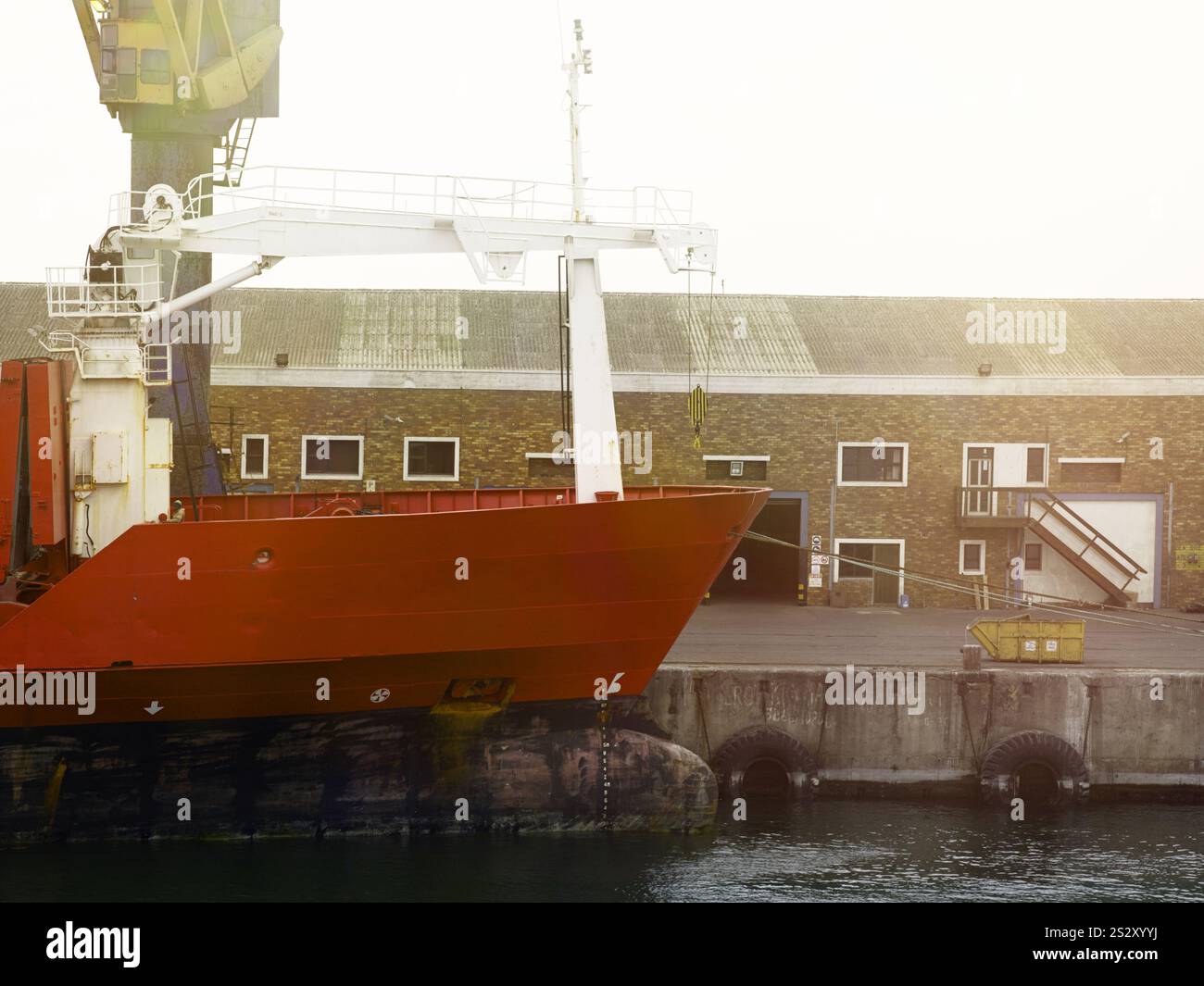 Scena portuale ndustriale con una nave dallo scafo rosso attraccata a Walvis Bay, Namibia, con attrezzature per il trasporto merci ed edifici portuali visibili. Foto Stock
