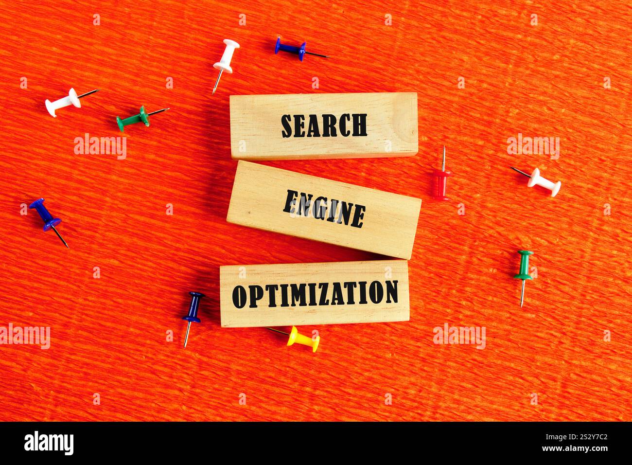 Tre blocchi di legno etichettati ricerca, motore e ottimizzazione sono visualizzati in modo creativo tra i pulsanti colorati su una superficie arancione vivace, evidenziata Foto Stock