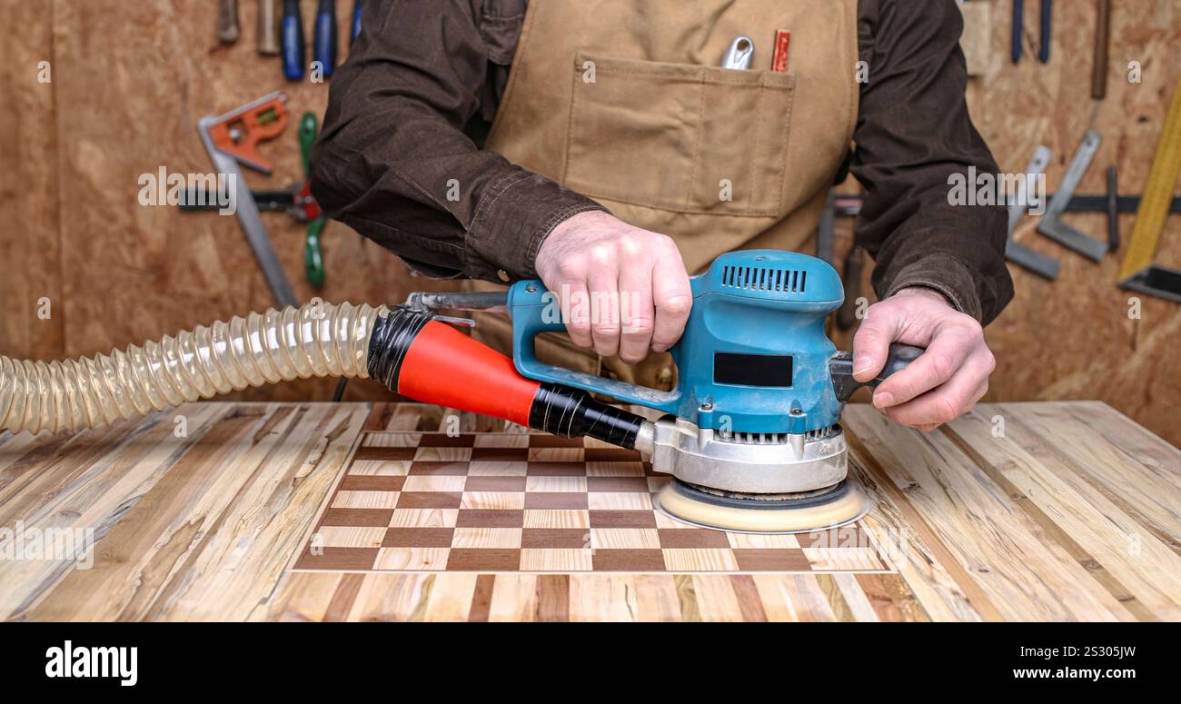 Levigatura di carpentiere scacchiera in legno in officina con levigatrice orbitale Foto Stock