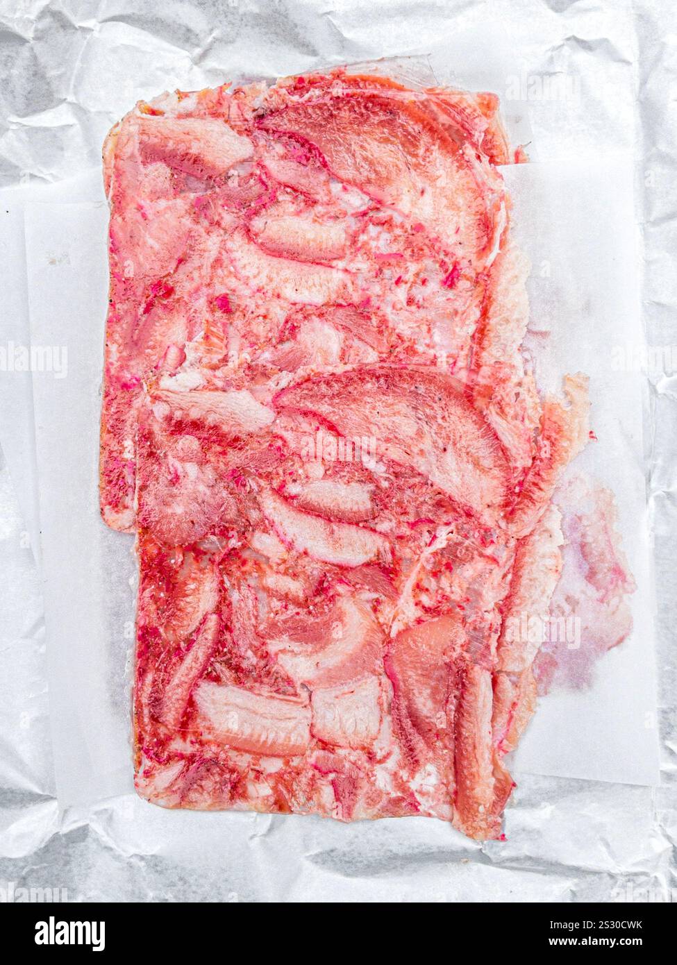 Primo piano di una terrina di maiale pressata esposta su un foglio di carta di cera, che mostra la sua consistenza marmorizzata e strati di carne e grasso. Foto Stock