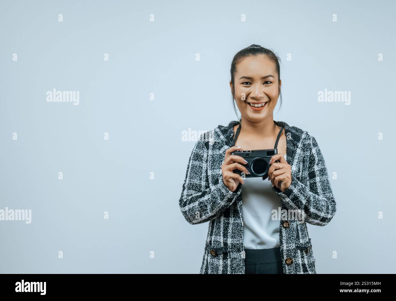 Ritratto di donna asiatica che indossa abiti casual con un grande sorriso sul viso, tenendo in mano una macchina fotografica per scattare una foto. Sfondo isolato in studio con vuoto Foto Stock