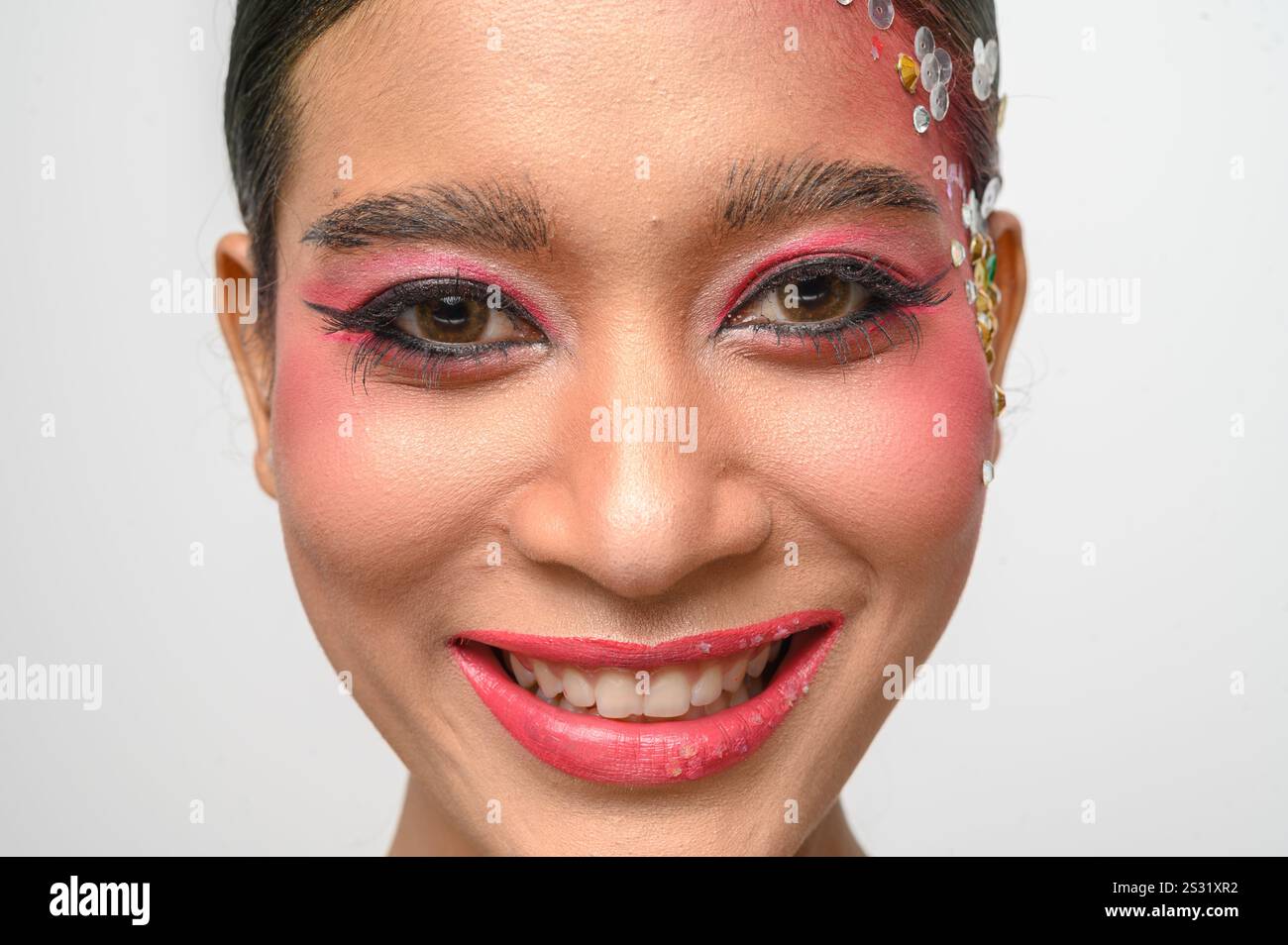 Donna che indossa trucco e decorazioni rosa sul viso. Isolato su sfondo bianco Foto Stock