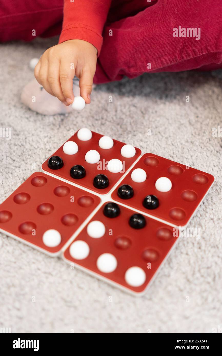 Una mano si sposta sopra il tabellone di gioco, tenendo in mano biglie bianche e nere. Il bambino è pronto a mettere le biglie, pensando attentamente alla prossima mossa. Foto Stock