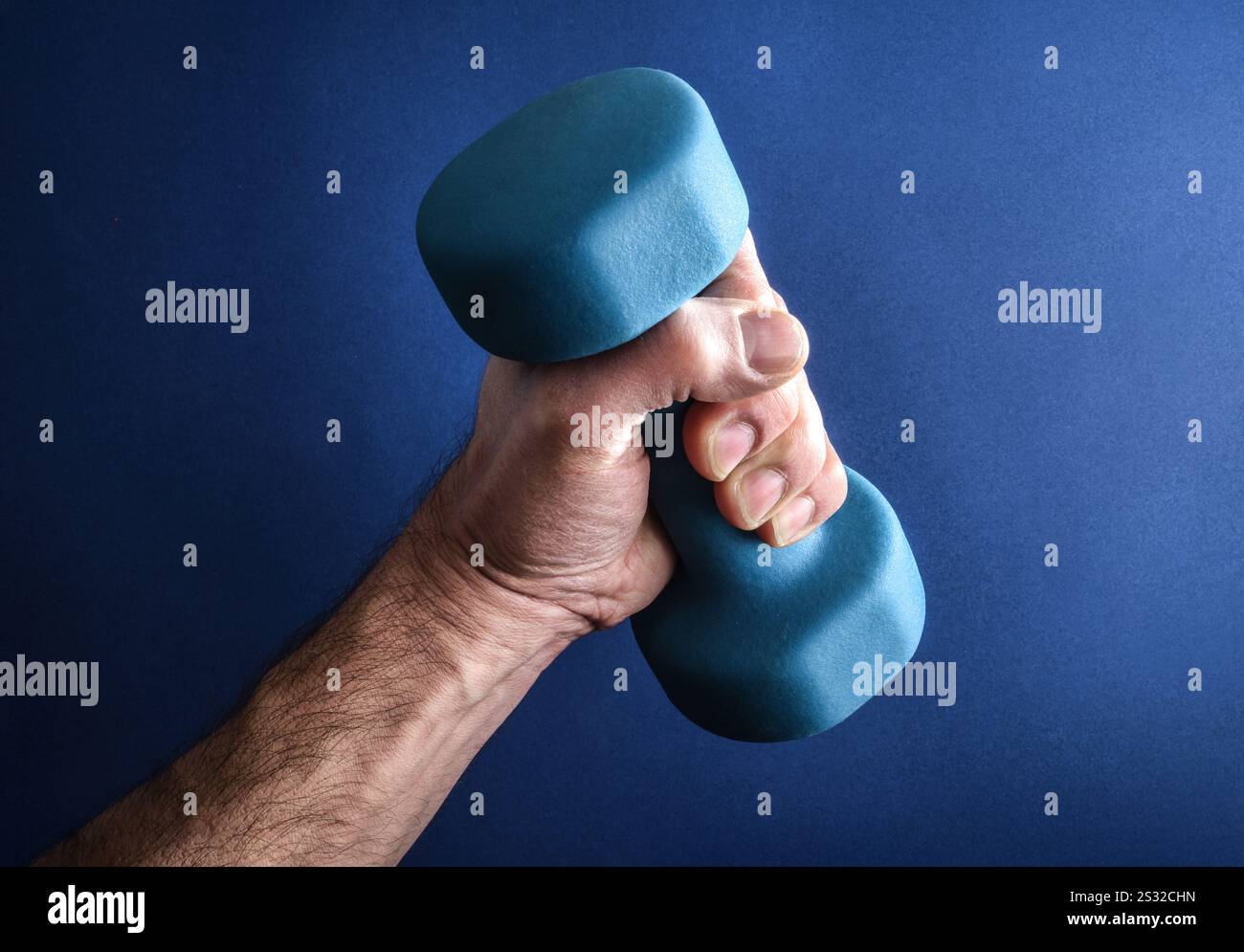 Dettaglio del braccio dell'uomo forte che solleva un manubrio in neoprene blu isolato su sfondo blu gradiente. Foto Stock