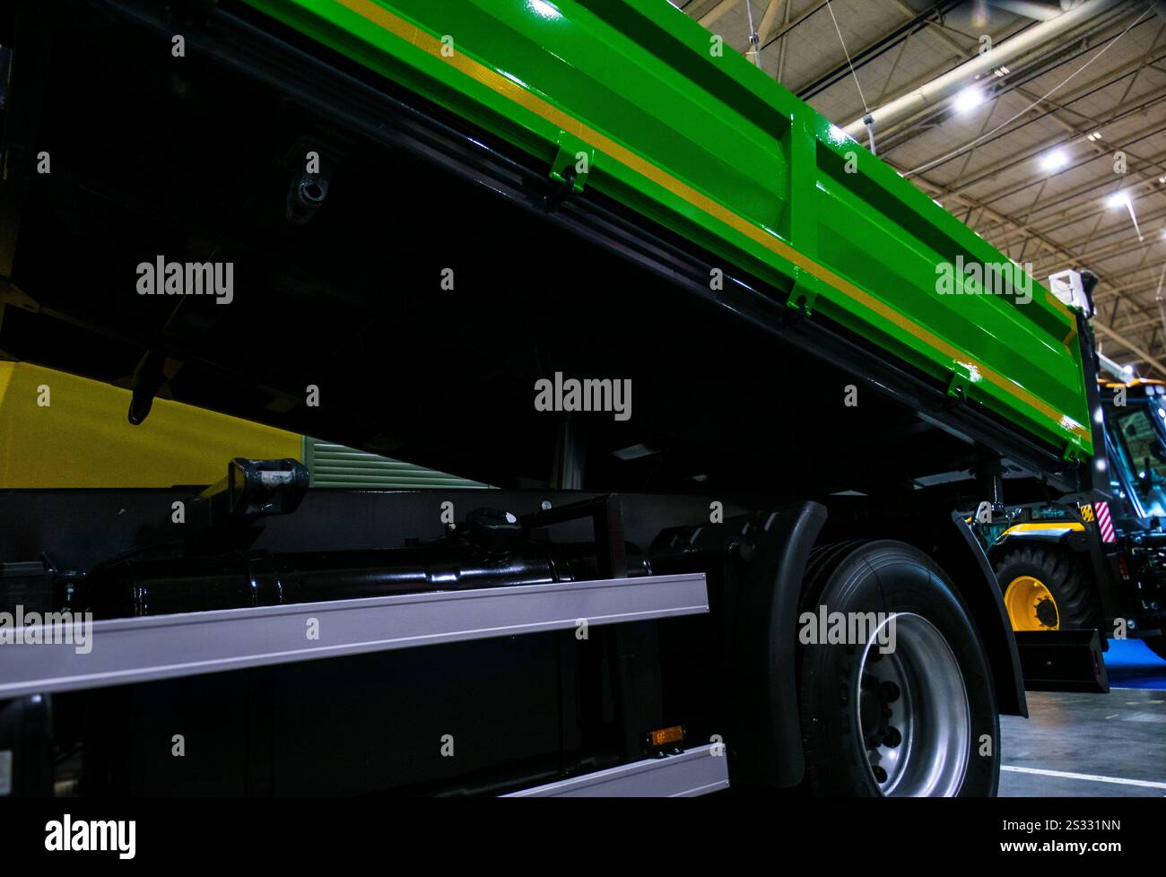 Un dumper verde è parcheggiato in un ambiente industriale. Il pianale del dumper viene sollevato con un'angolazione ripida, rivelando la struttura in metallo e l'impianto idraulico Foto Stock