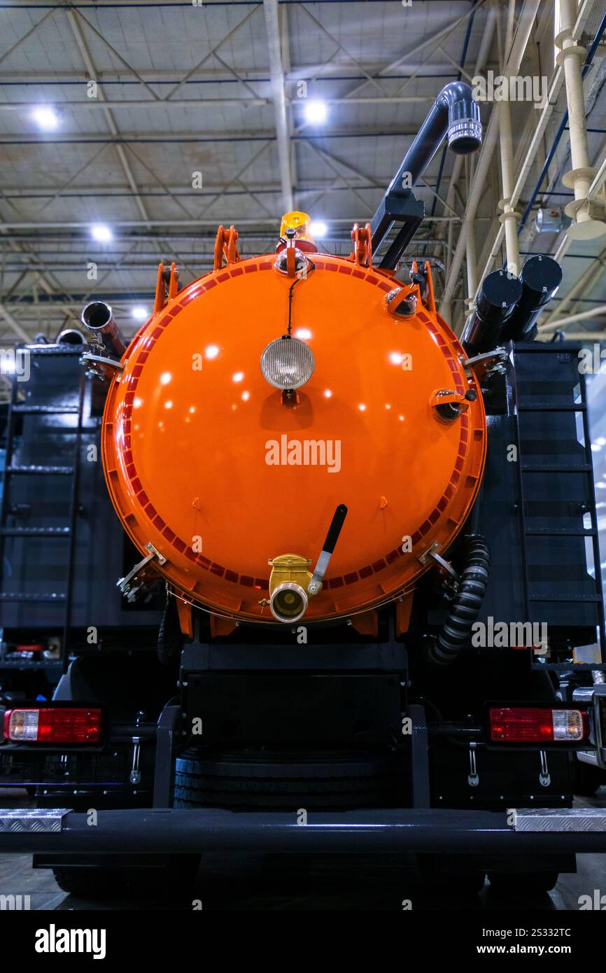 Vista posteriore ravvicinata di un carrello a vuoto, noto anche come autocisterna sottovuoto o aspiratore a pozzetto, dotato di un grande serbatoio arancione brillante. Foto Stock
