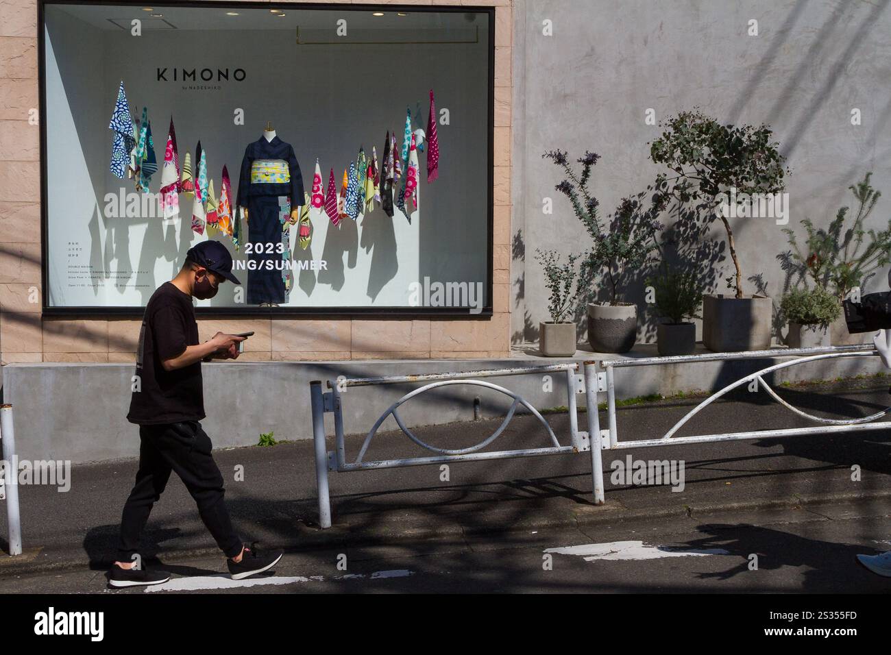 Un giovane giapponese, che usa uno smartphone, passa davanti a un negozio con kimono nella vetrina. Harajuku, Tokyo, Giappone. Foto Stock