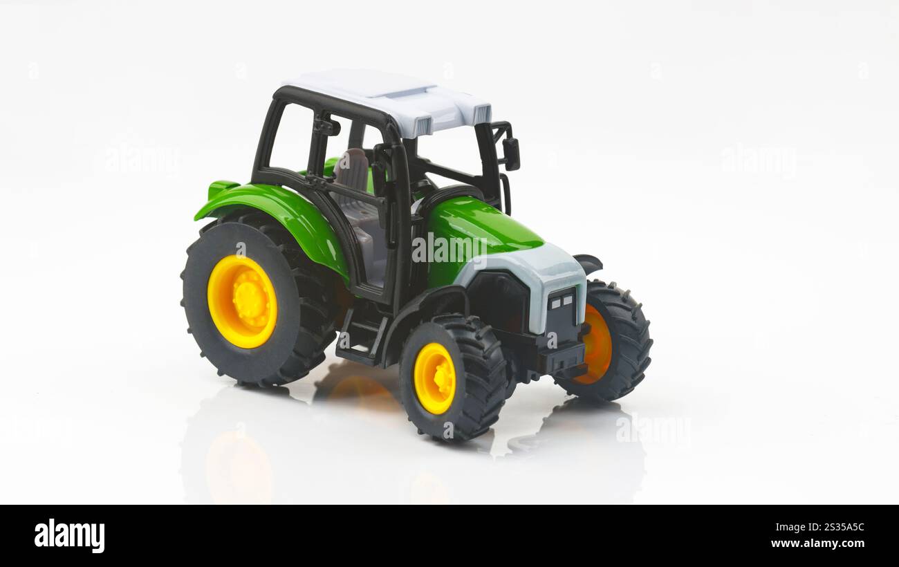 Trattore giocattolo verde isolato su sfondo bianco che riflette sulla superficie, che rappresenta l'agricoltura e l'agricoltura Foto Stock