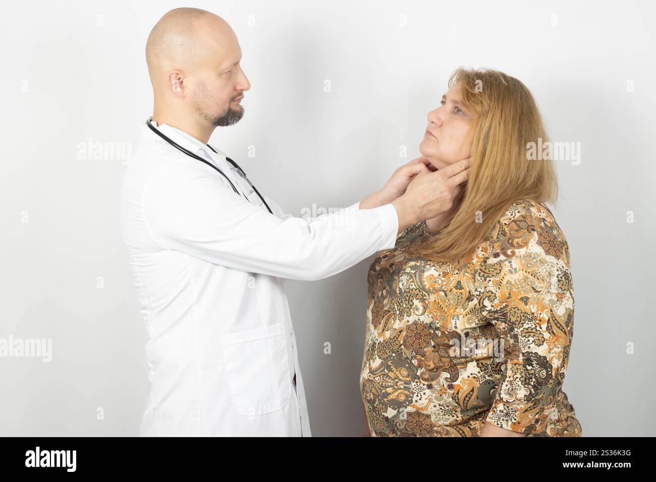Un medico di sesso maschile con un camice bianco e uno stetoscopio esamina il collo di una paziente di sesso femminile. Foto Stock