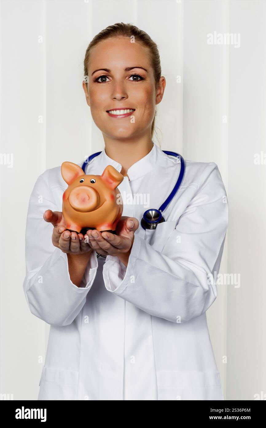Un giovane medico ha in mano un salvadanaio. Foto simbolica per le tasse del medico, apertura di uno studio e assicurazione pensionistica. Austria Foto Stock