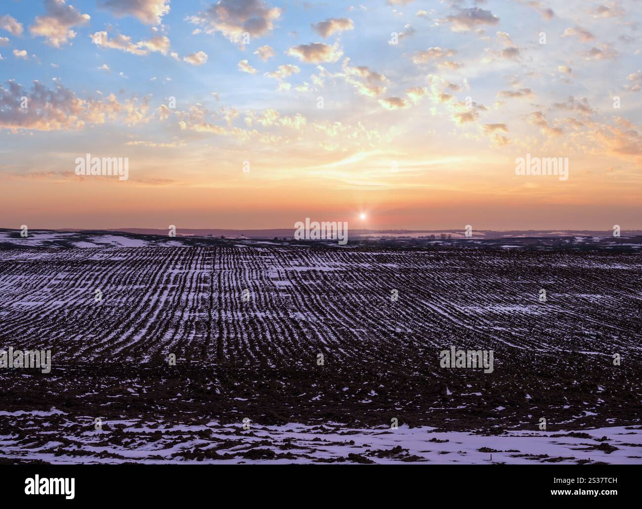 Terra nera, terra arabile coperta dall'ultima neve, primavera primaverile. Calmo tramonto serale nella campagna Ucraina, regione di Lviv. Foto Stock