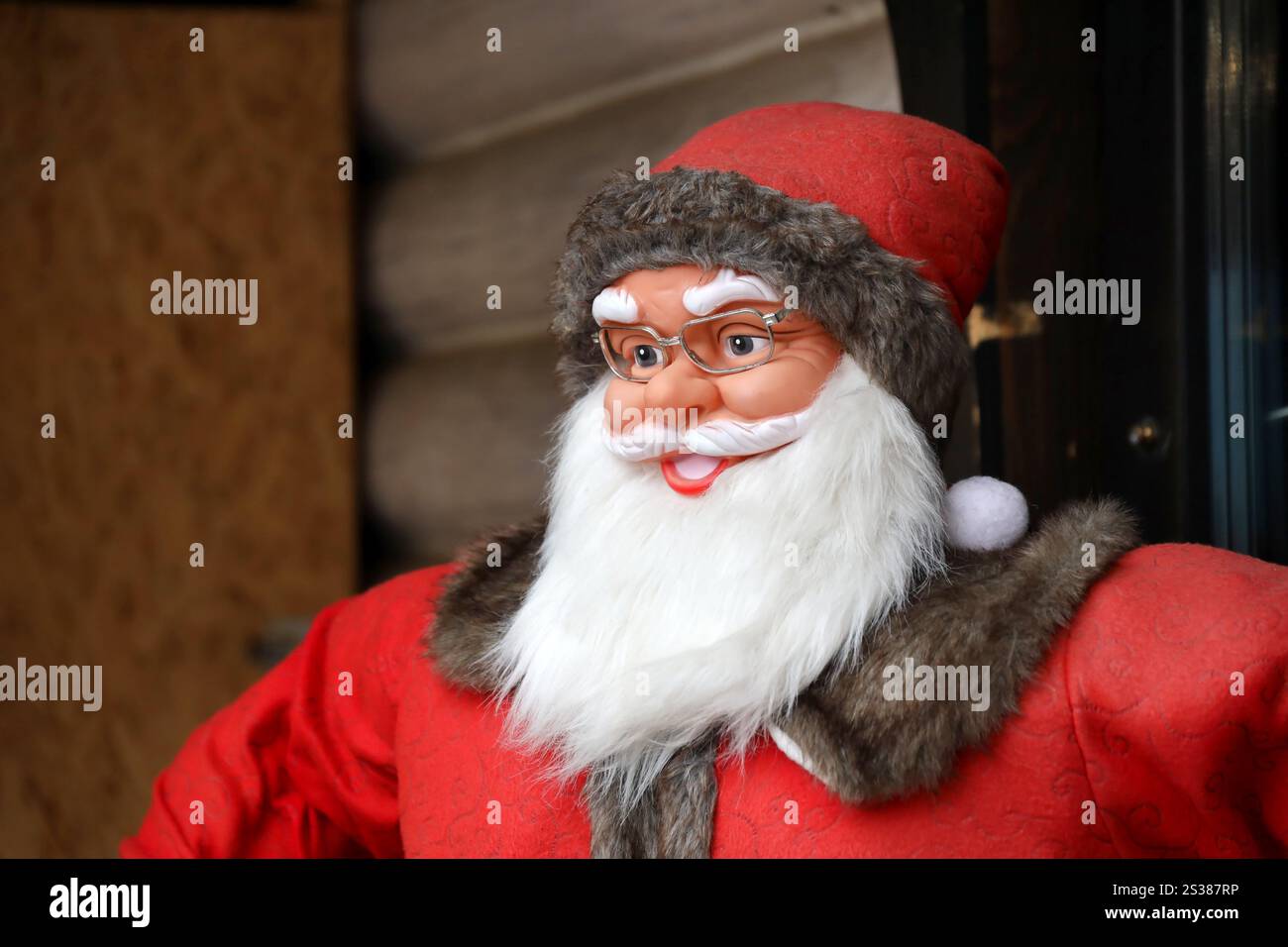 Grande figura di plastica di Babbo natale con abiti classici e cappello di babbo natale vicino alla casa di legno. Grande personaggio di plastica di Babbo natale con abiti classici di babbo natale Foto Stock