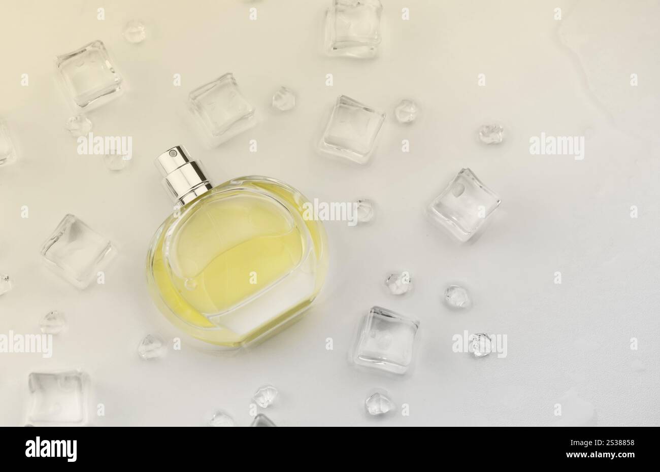Bottiglia gialla di profumo femminile, fotografia obiettivo della bottiglia di profumo in cubetti di ghiaccio e acqua su un tavolo bianco. Vista dall'alto. Foto del prodotto mockup, Foto Stock