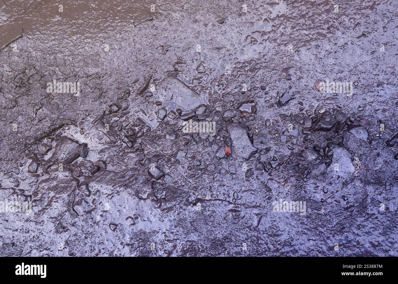 Primo piano di pozzanghere fangoso con piccole pietre sulla superficie bagnata. Trama di sfondo. Primo piano di pozzanghere fangoso con piccole pietre sulla superficie bagnata. Sfondo Foto Stock