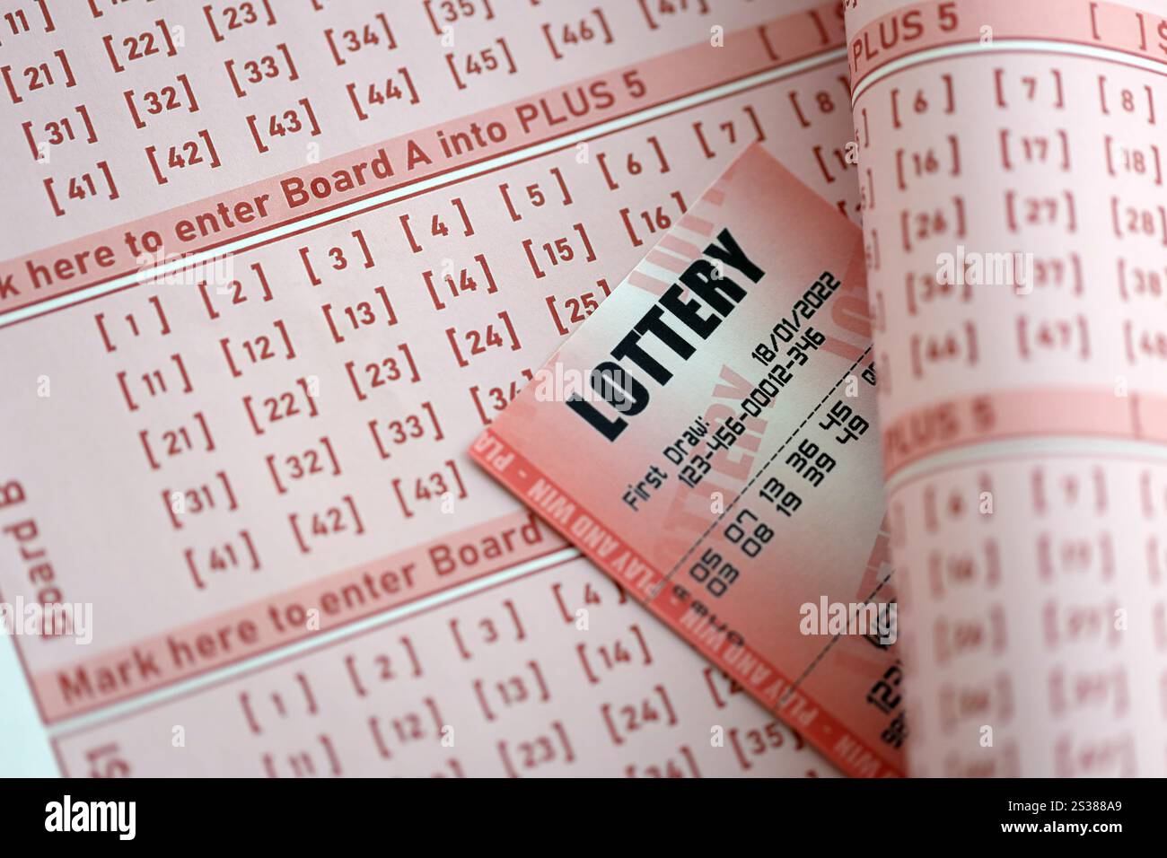 Il biglietto della lotteria rossa si trova su fogli da gioco rosa con i numeri da contrassegnare per giocare alla lotteria. Concetto di gioco alla lotteria o dipendenza dal gioco d'azzardo. Primo piano Foto Stock