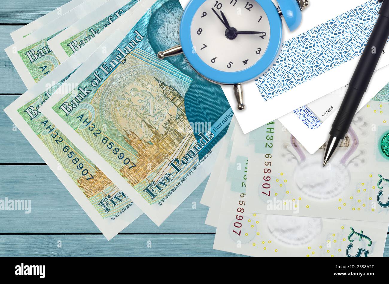 Banconote da 5 sterline inglesi e sveglia con penna e buste. Concetto di stagione fiscale, termine di pagamento per credito o prestito. Operazioni finanziarie utilizzando Foto Stock