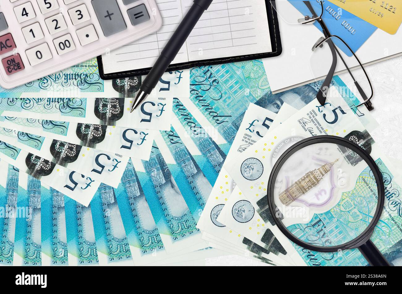 Banconote da 5 sterline inglesi e calcolatrice con occhiali e penna. Concetto di stagione del pagamento delle imposte o soluzioni di investimento. Alla ricerca di un lavoro con stipendio elevato Foto Stock