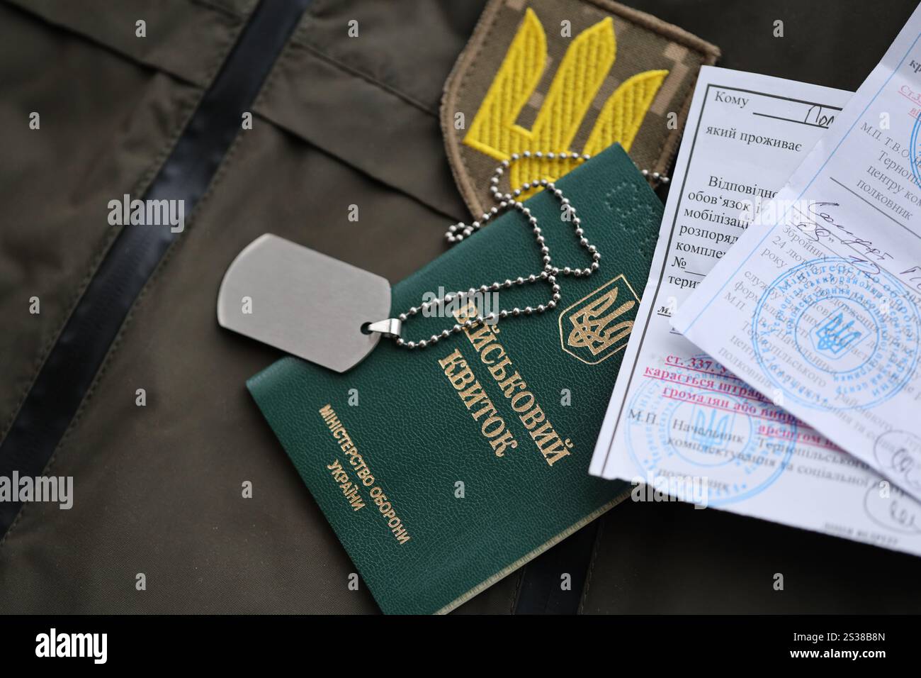 Gettone militare o biglietto d'identità dell'esercito con avviso di mobilitazione si trova sull'uniforme militare ucraina verde in casa da vicino. Gettone militare o tessera militare Foto Stock