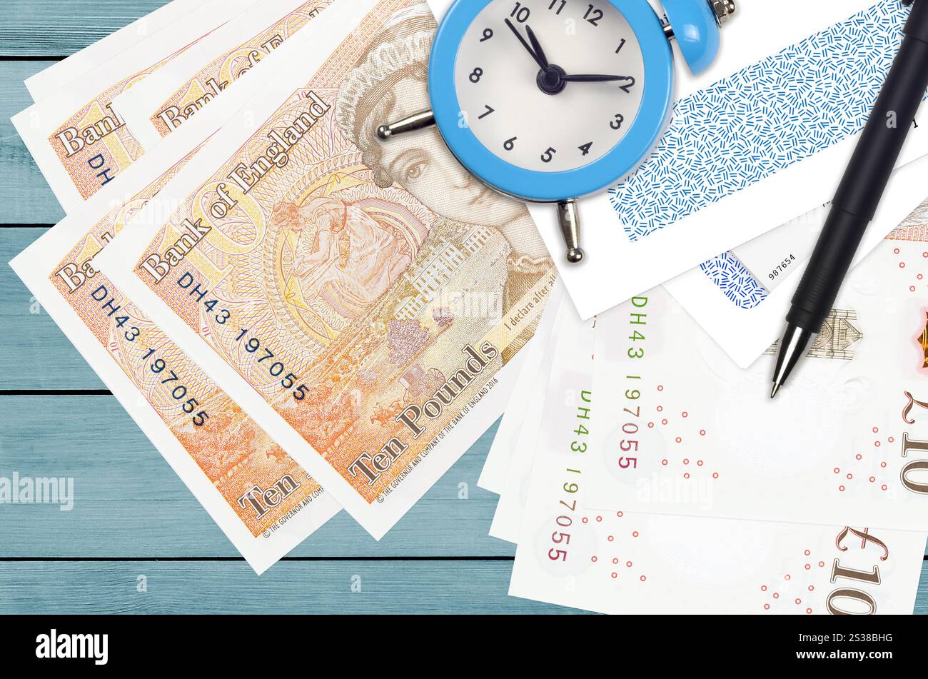 Bollette da 10 sterline britanniche e sveglia con penna e buste. Concetto di stagione fiscale, termine di pagamento per credito o prestito. Operazioni finanziarie utilizzando Foto Stock