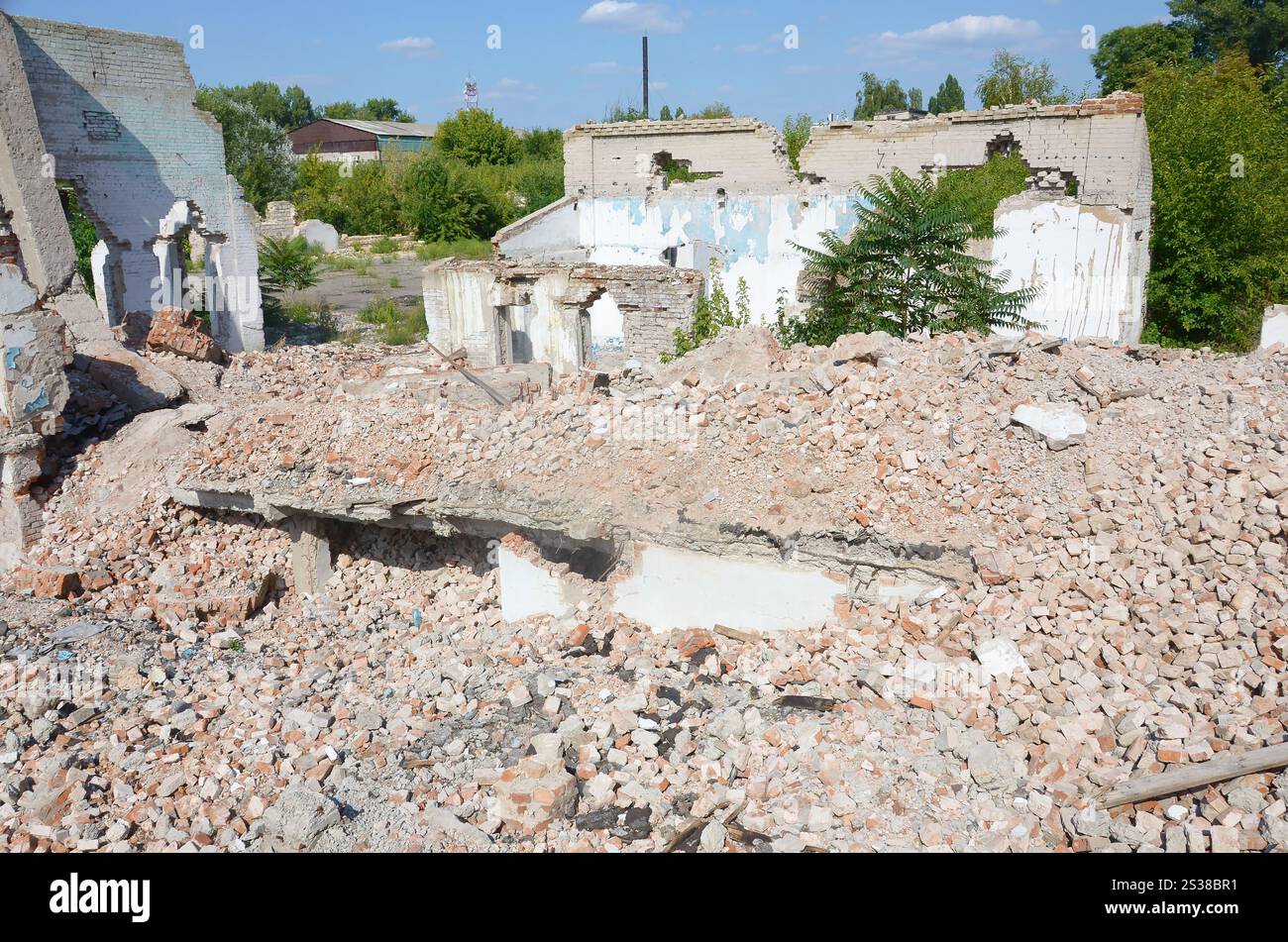 Edificio industriale a più piani crollato di giorno. Scena del disastro piena di detriti, mattoni rotti e case non residenziali danneggiate. Concetto di guerra Foto Stock