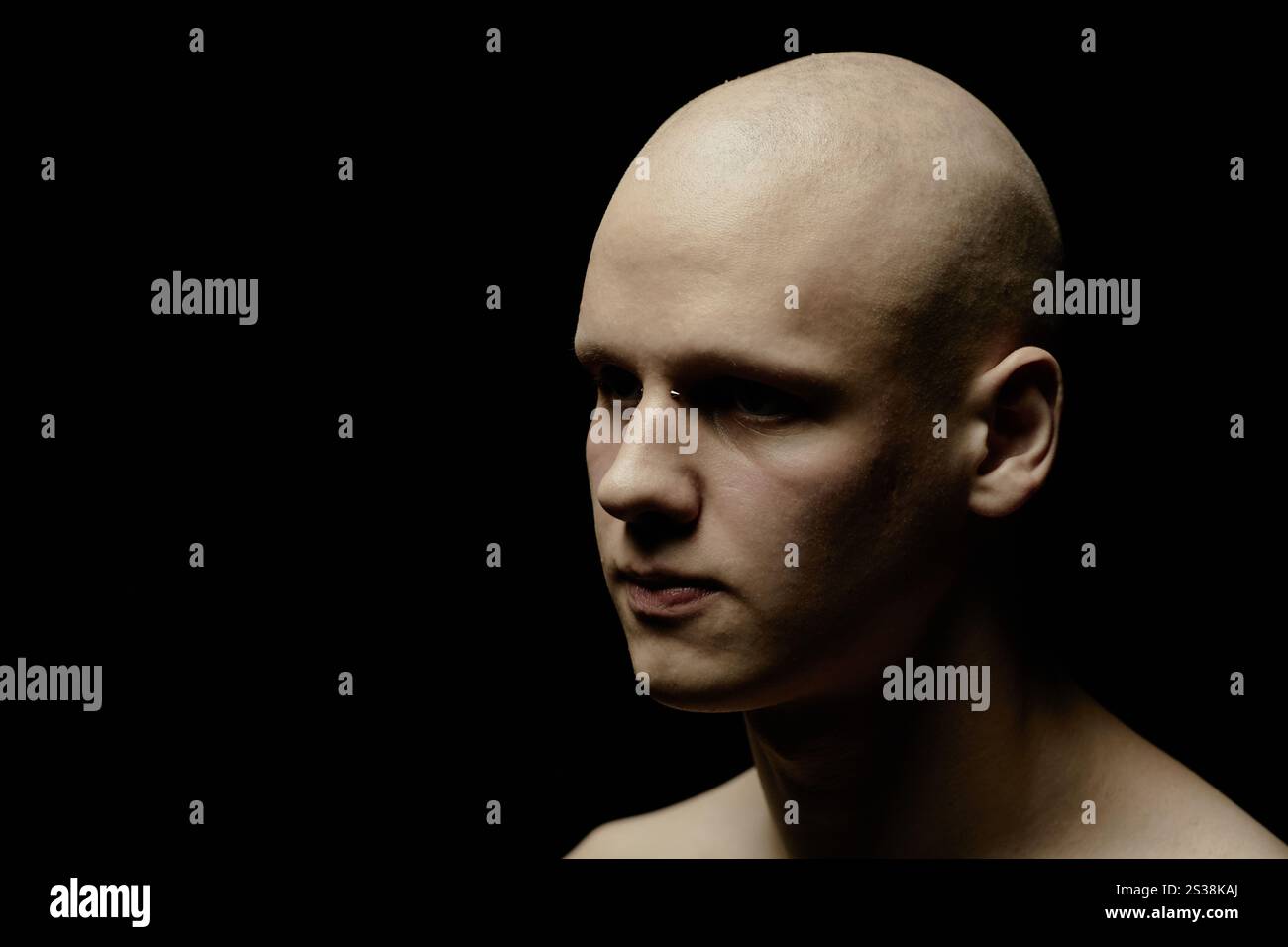 Ritratto di un uomo calvo pallido con il ponte che trasuda l'estetica industriale che guarda nel vuoto mentre stai in piedi in uno studio illuminato a chiave bassa su sfondo nero, copia spazio Foto Stock