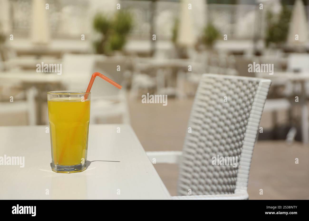 Bicchiere di succo d'arancia con paglia di plastica su un tavolo bianco nella zona lounge all'aperto del ristorante con tempo soleggiato. Bicchiere di succo d'arancia con cannuccia di plastica Foto Stock