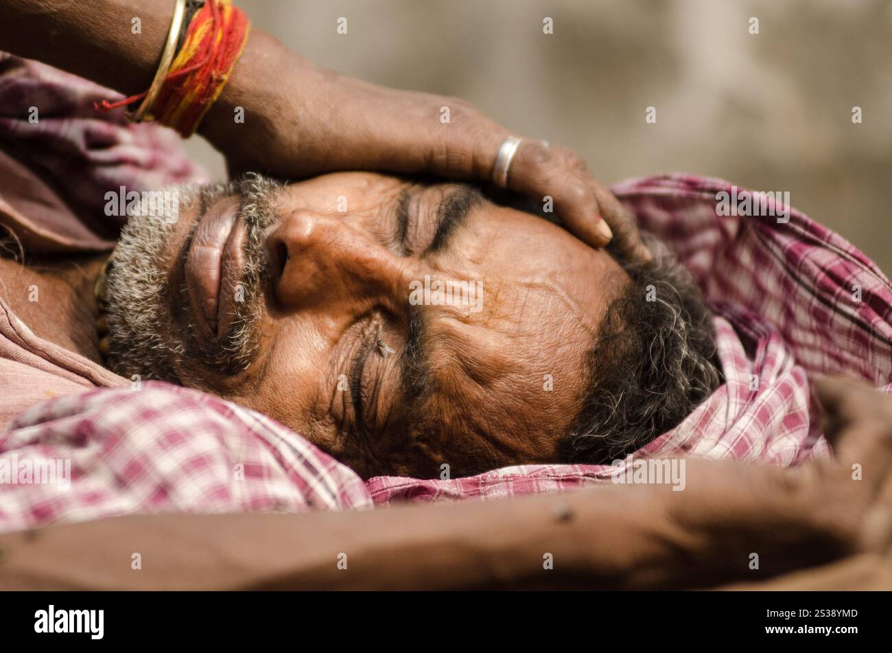 L'uomo riposa contro un muro, mostrando segni di stanchezza e recupero in un ambiente informale durante il giorno nelle zone rurali Foto Stock
