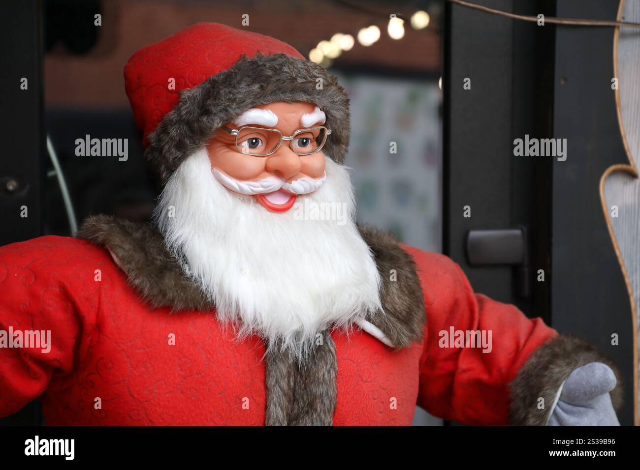 Grande figura di plastica di Babbo natale con abiti classici e cappello di babbo natale vicino alla casa di legno. Grande personaggio di plastica di Babbo natale con abiti classici di babbo natale Foto Stock