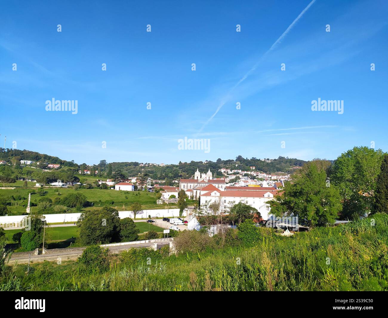 Una vista pittoresca di un pittoresco villaggio con tetti di tegole rosse accoccolati tra verdi colline e sotto un cielo blu luminoso, che mostra la serena bellezza di Foto Stock