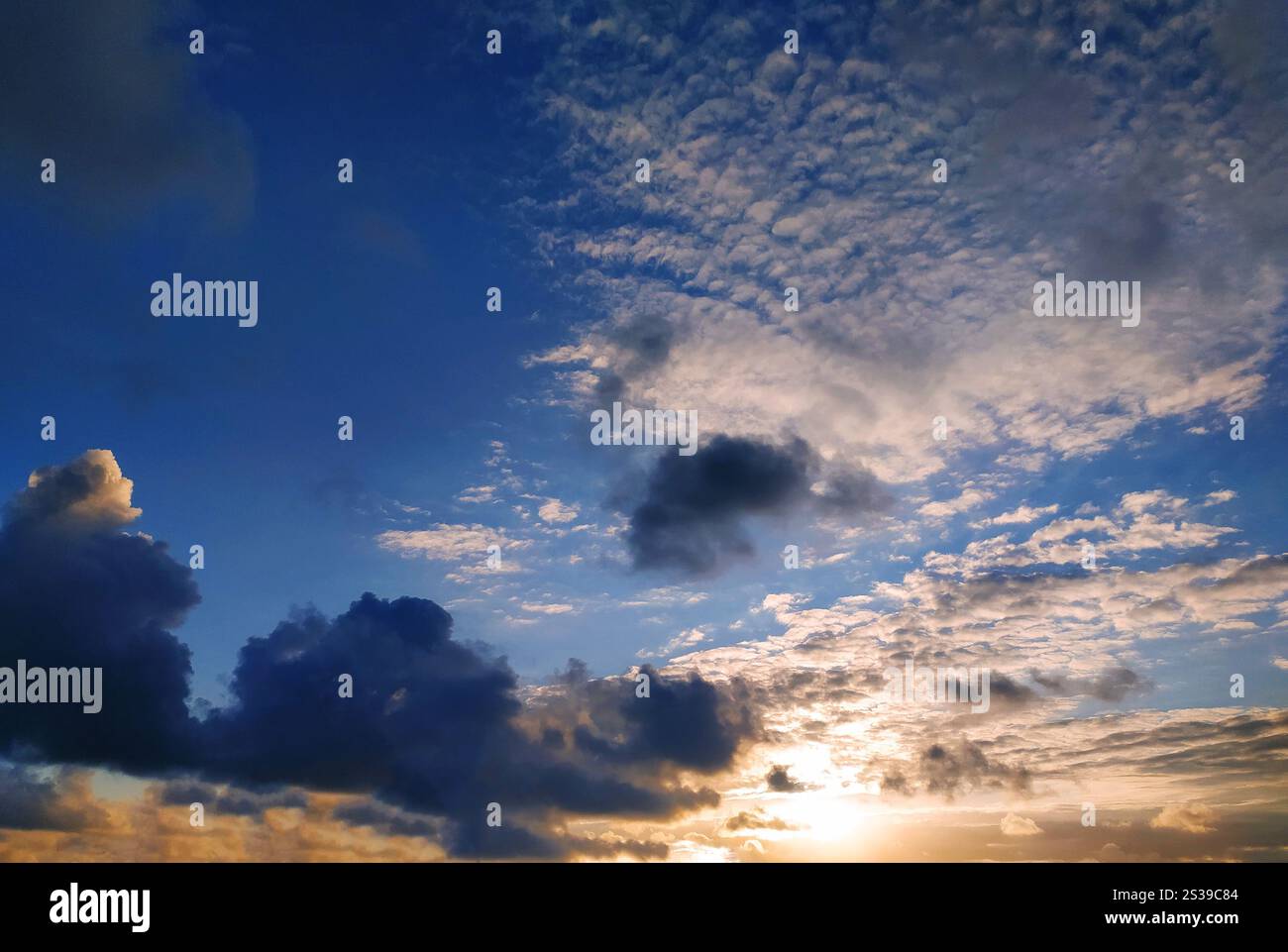 Il sole sta tramontando, proiettando un caldo bagliore sulle nuvole del cielo. I colori vibranti del tramonto si riflettono nelle nuvole, creando un'atmosfera drammatica Foto Stock