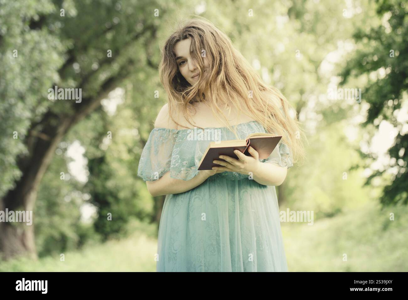 una donna elegante legge un libro che cammina in un prato Foto Stock