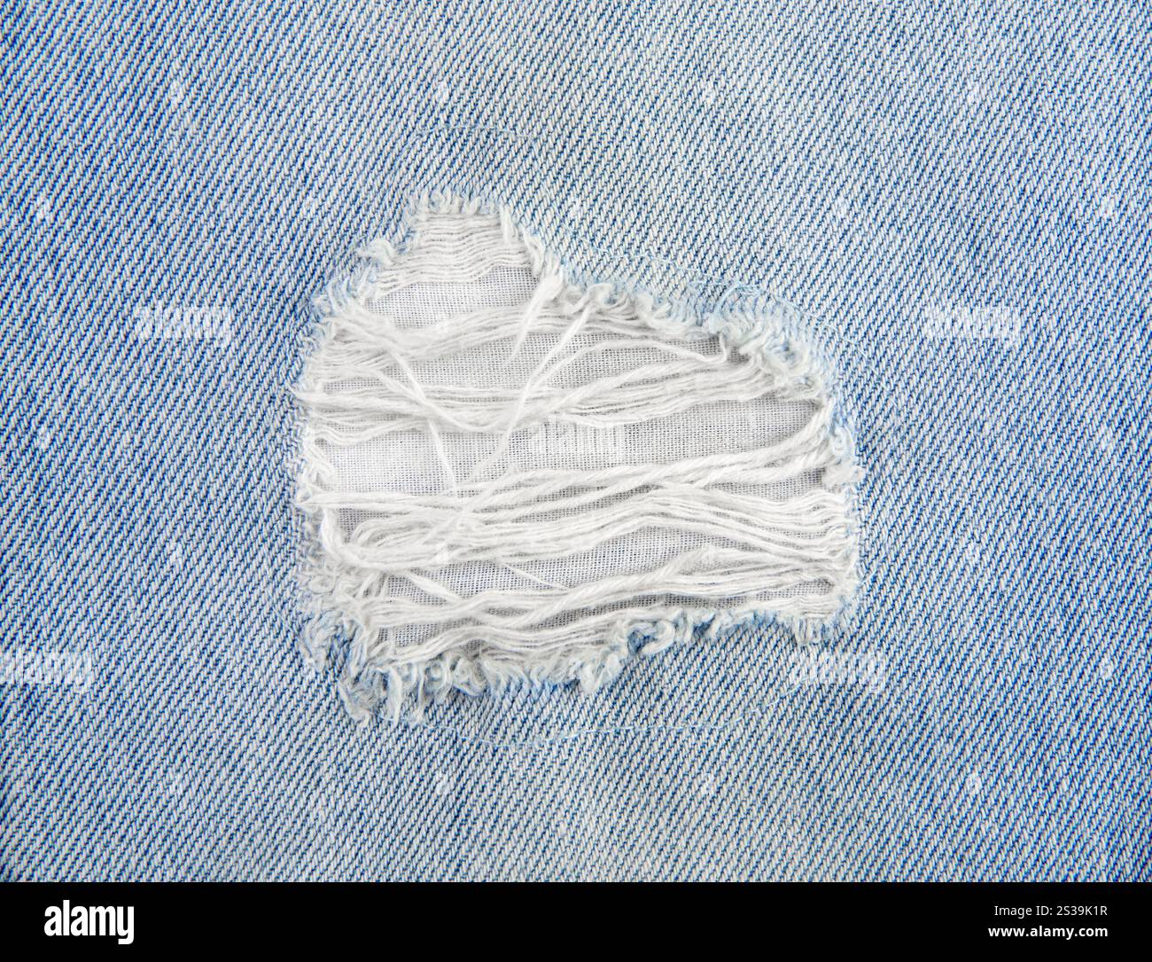 Vista ravvicinata dei jeans in denim azzurro con buco strappato. Vista orizzontale, ripresa in studio, ampio spazio di copia. Foto Stock