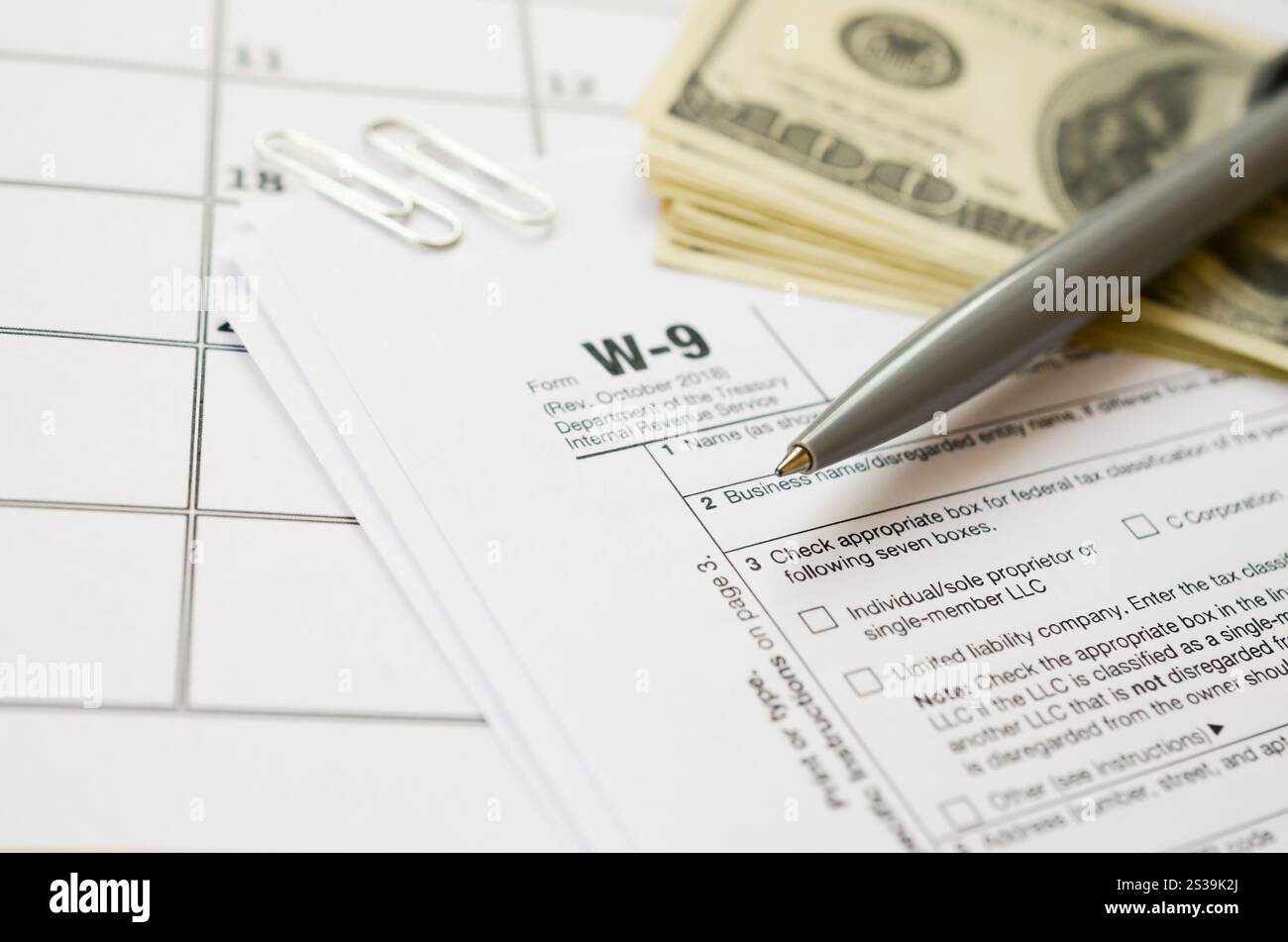 Modulo IRS W-9 richiesta di numero di identificazione contribuente e certificato vuoto si trova con la penna e molte banconote da cento dollari sulla pagina del calendario. Tassa Foto Stock