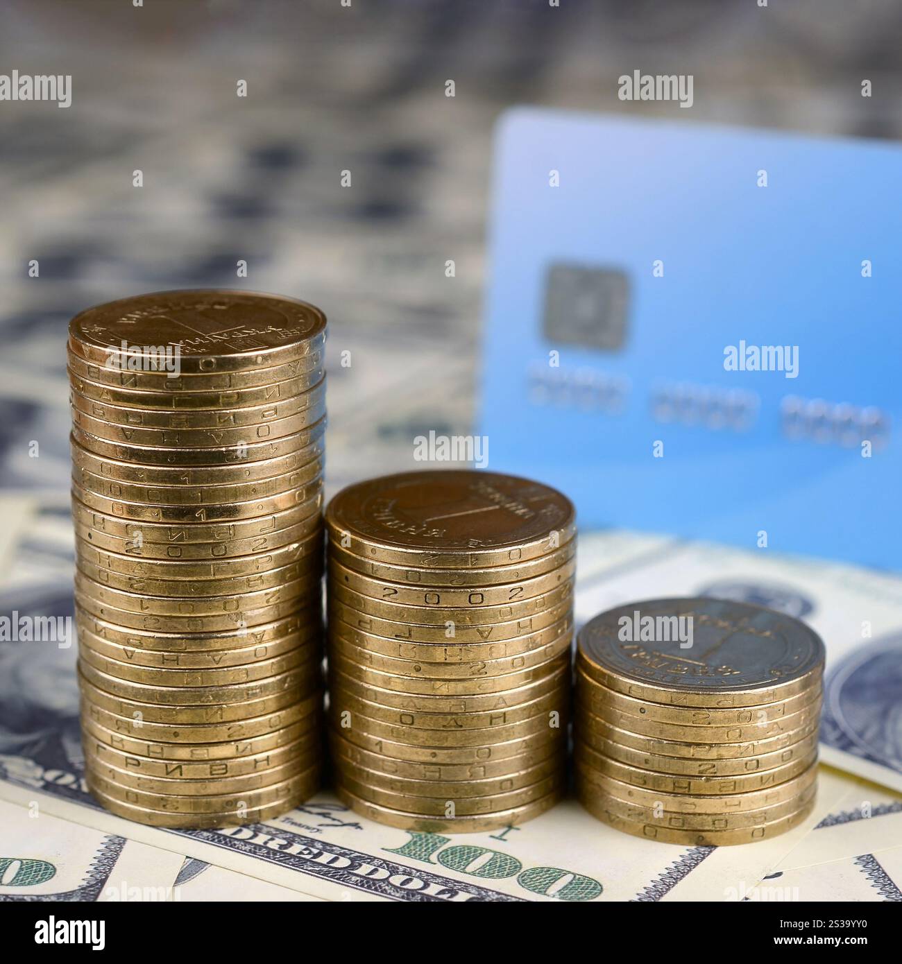 Monete ucraine e carta di credito blu chiudono su una grande pila di banconote da cento dollari. Valuta dell'Ucraina. Saldo del denaro e scambio online Foto Stock