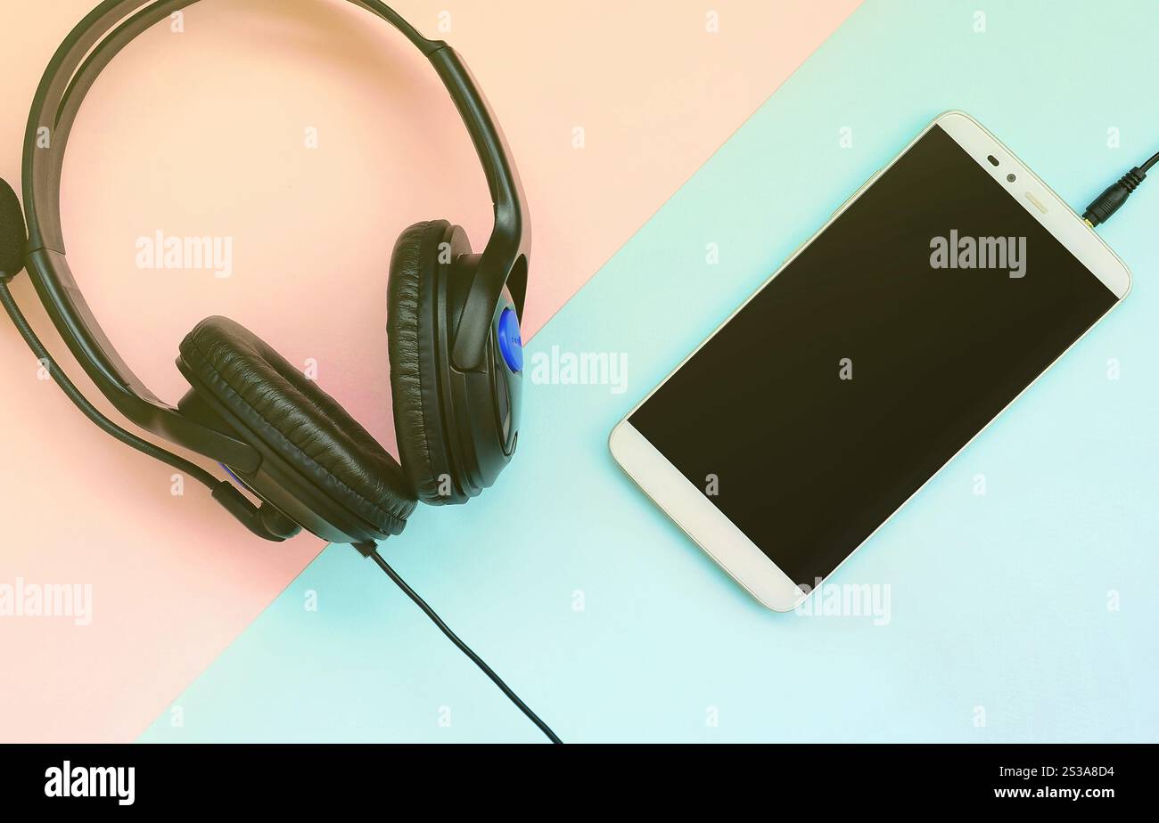 Le cuffie e lo smartphone neri si trovano su un colorato sfondo viola pastello. Concetto di ascolto musicale. Tecnologia portatile. Vista dall'alto in posizione piatta. Nero Foto Stock
