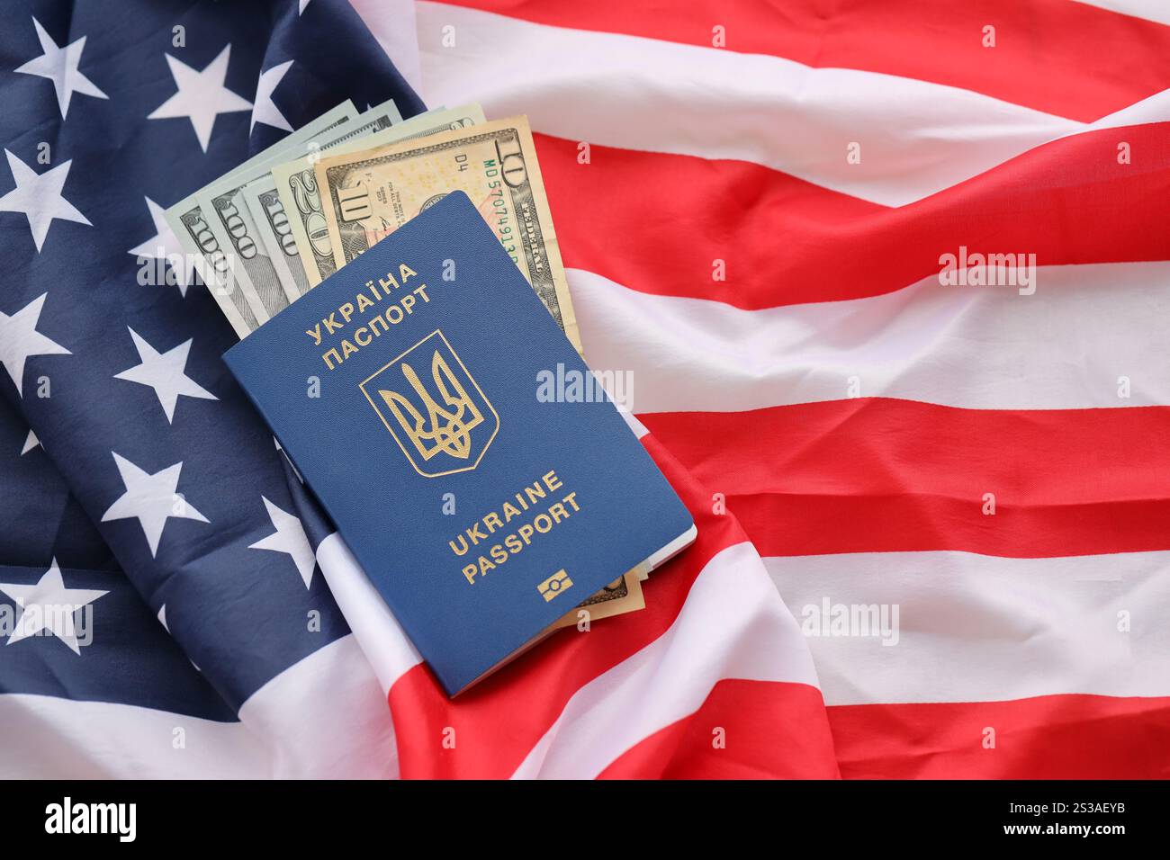 Passaporto biometrico ucraino e banconote in dollari USA sulla bandiera ondulata degli Stati Uniti d'America da vicino. Passaporto biometrico ucraino e Stati Uniti Foto Stock