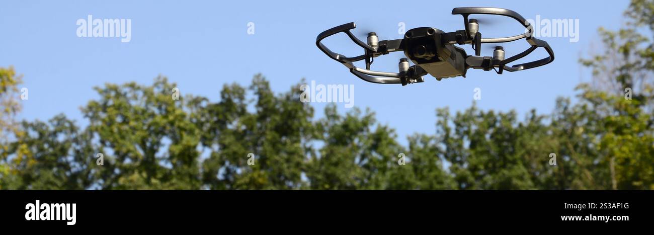 Drone con fotocamera decolla dalla terraferma e vola per scattare foto aeree al tramonto davanti agli alberi. Drone con fotocamera decollo da Foto Stock
