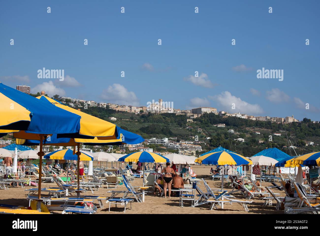 Spiaggia italiana con lettini, ombrelloni, rilassanti vacanzieri, costa soleggiata, mare vivace, atmosfera estiva. Foto Stock